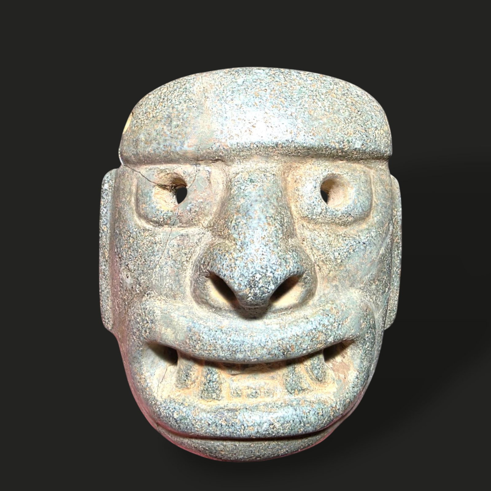 Pre-Columbian Chavin stone mask: Pre-Columbian stone mask, possibly from the Chavín culture of ancient Peru, dating between 900–200 BCE. The mask is intricately carved from a greenish-gray stone, featuring exaggerated facial featu