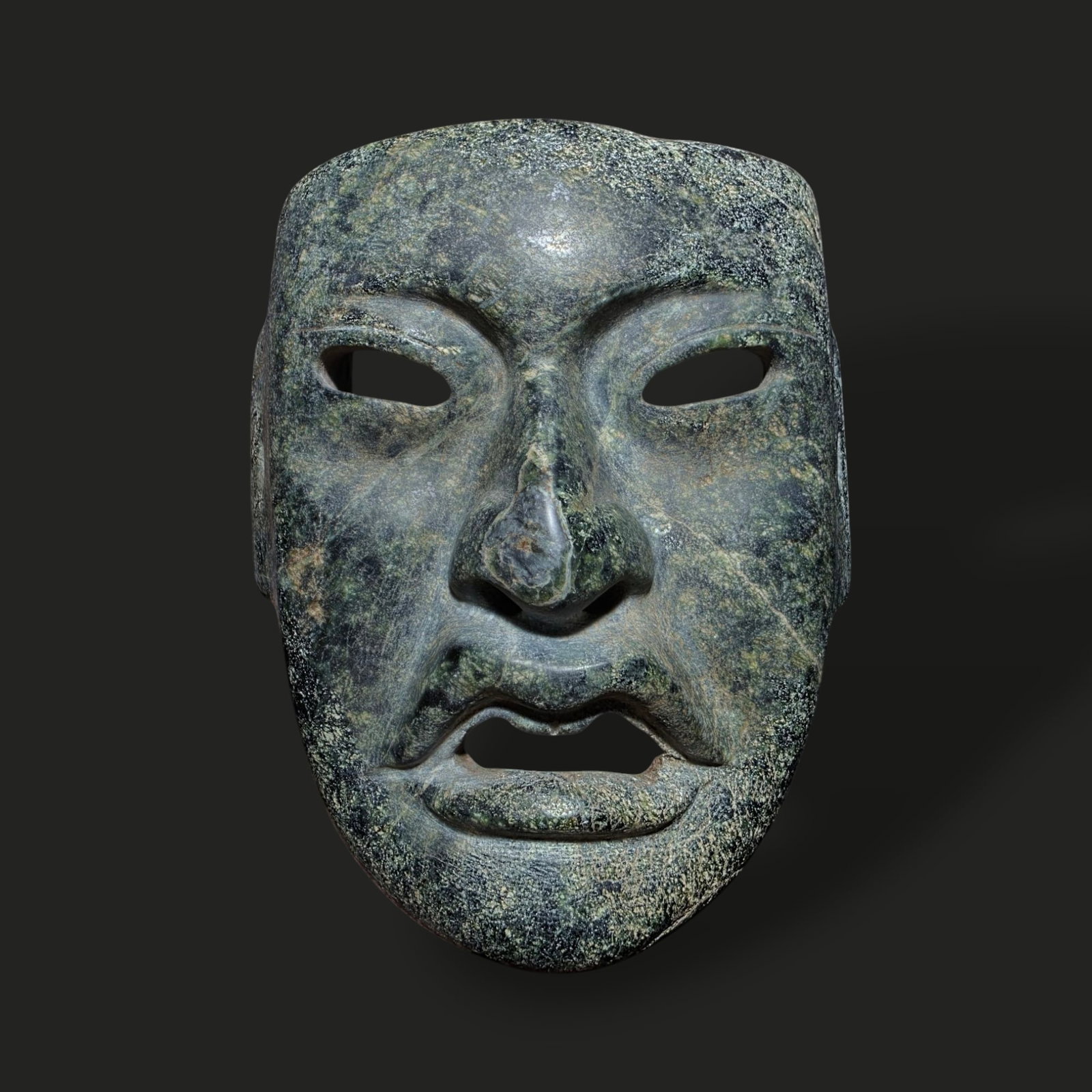 Pre-Columbian Olmec serpentine mask: Pre-Columbian Olmec serpentine mask, 1200–400 BCE, originating from Mesoamerica, particularly the Olmec heartland in present-day Mexico. Carved from greenish serpentine stone, the mask features a hi