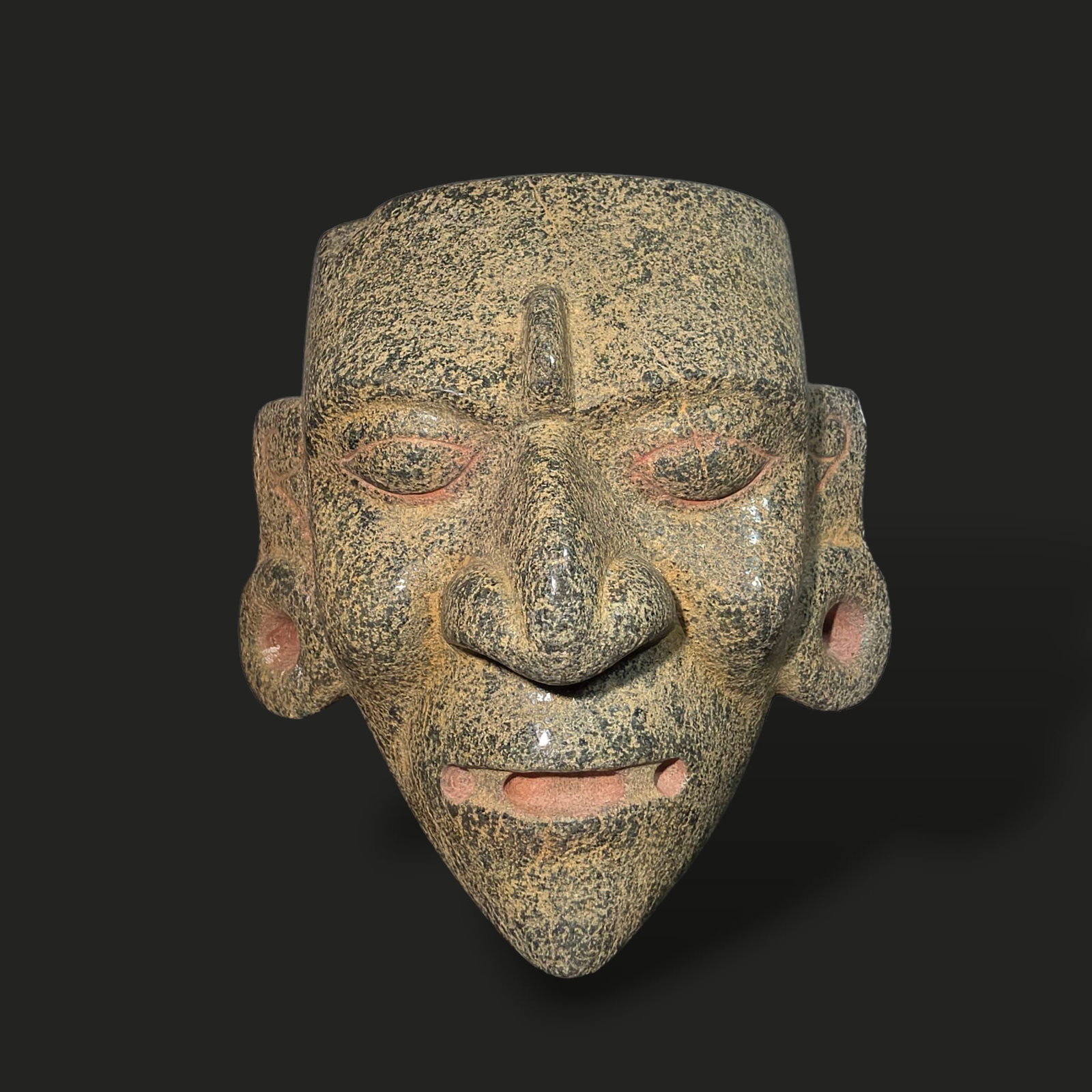 Pre-Columbian Mayan green stone mask: Pre-Columbian Mayan green stone mask, 600–900 CE, during the Late Classic period of the Maya civilization. Carved from speckled green stone, the mask features an angular facial structure with a prom