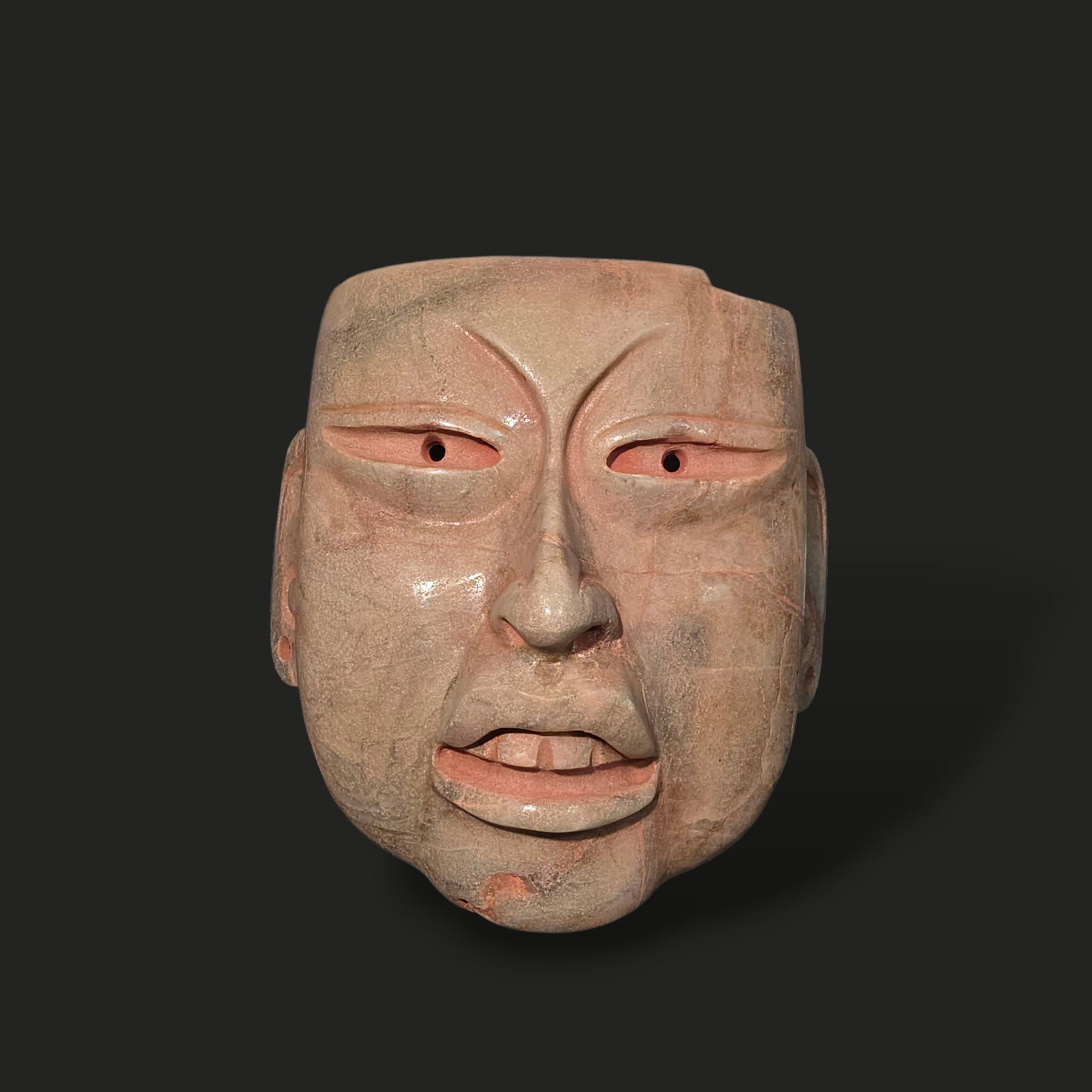 Pre-Columbian Olmec jade mask: Pre-Columbian Olmec mask, carved from jade, exhibits the refined artistry and symbolic depth characteristic of the Olmec civilization. The mask features a highly stylized human face with a strong, bro