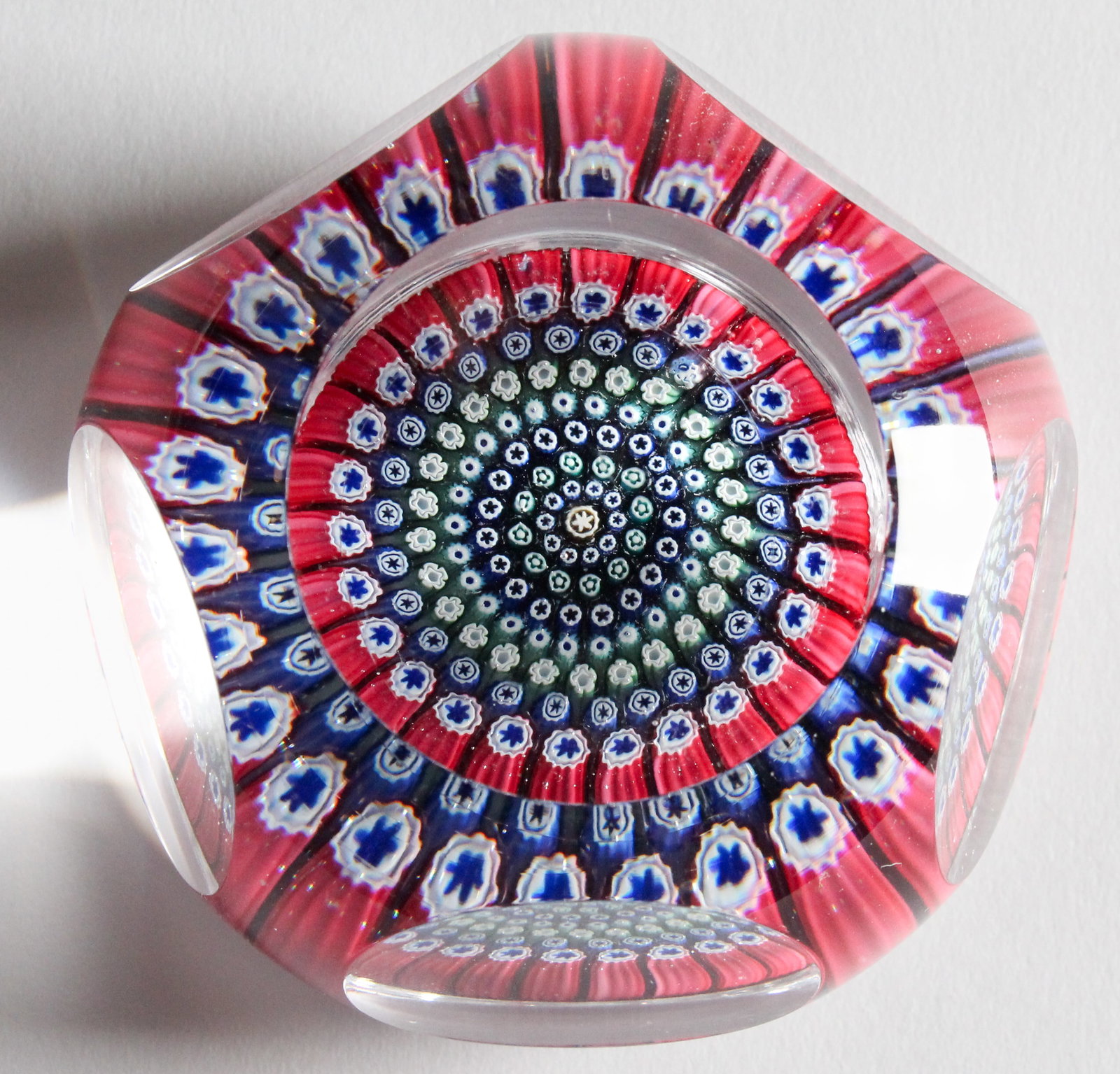 Whitefriars Concentric Millefiori Art Glass Paperweight, 1971: Description: A central floret cane is surrounded by seven rows of blue, black, green and red cog and star canes, the canes in each row becoming progressivey larger in size from the center blue to the 