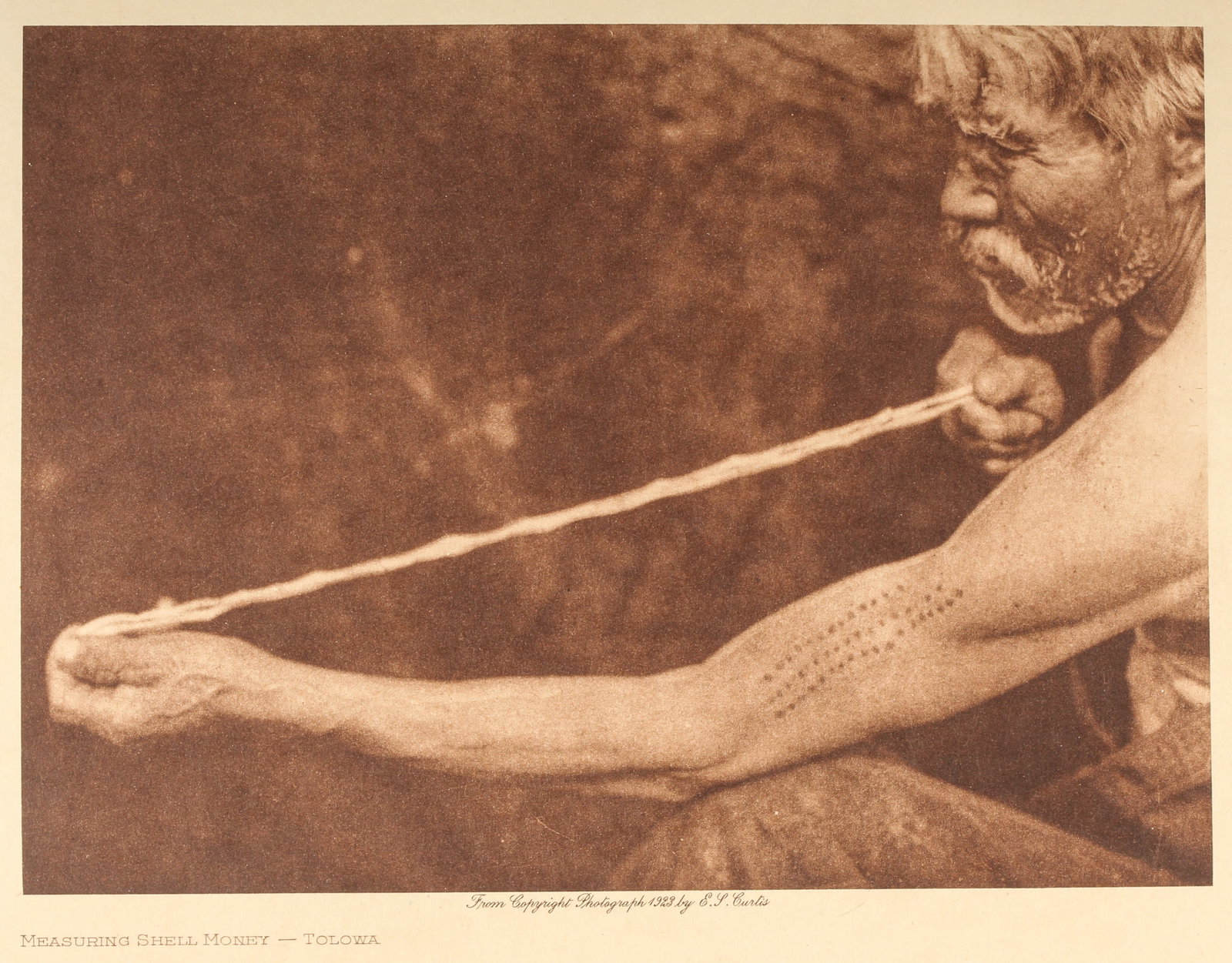 Edward S. Curtis (American, 1868-1952) Photogravure, Measuring Shell Money - Tolowa, 1923: Description: An Edward Curtis photogravure from the 1923 copyright photograph. As part of his "The North American Indian" portfolio 1907-1930. Museum specification framed/matted Title: Measuring Shell