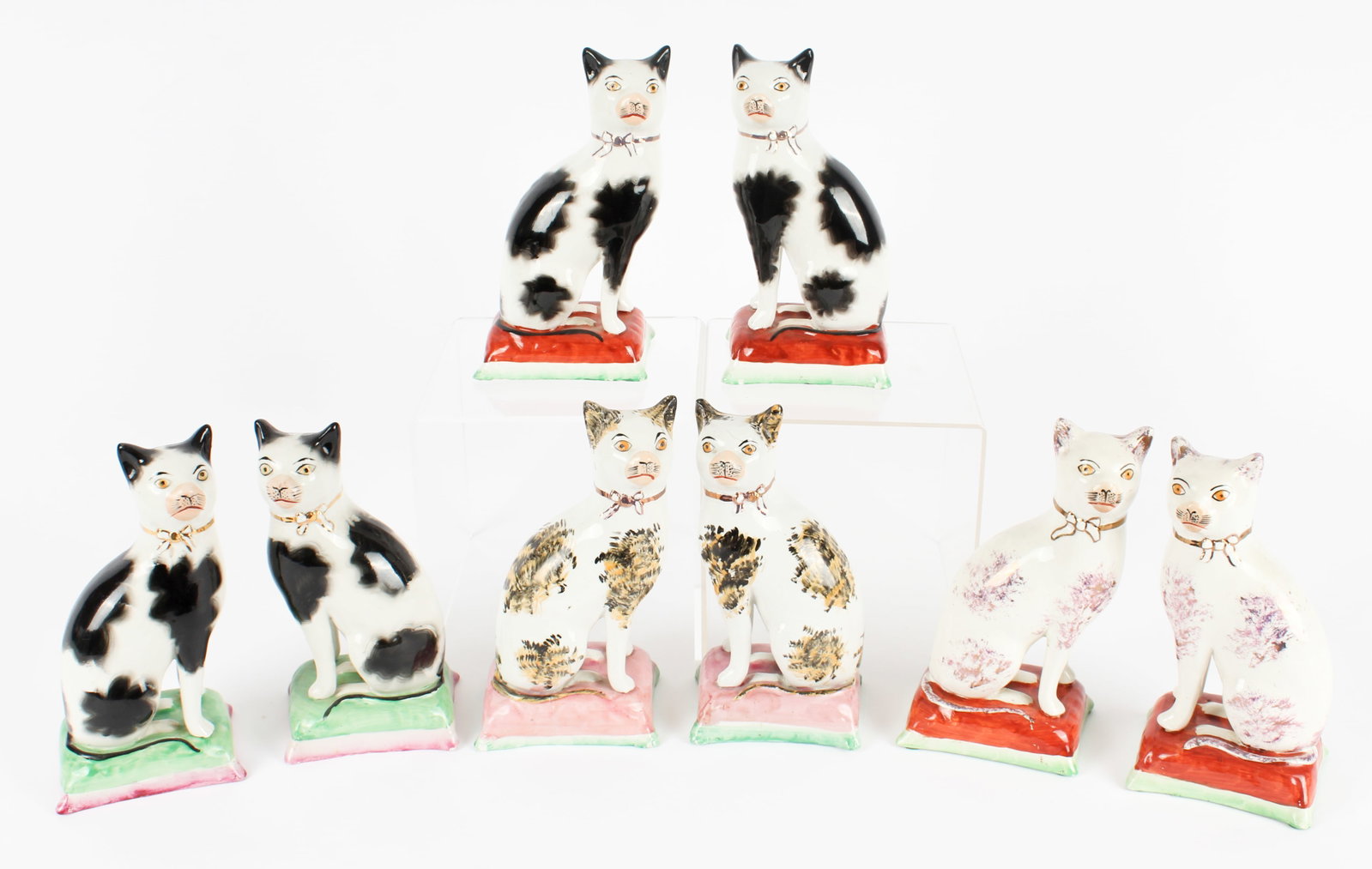 Eight Late 19th Century Staffordshire Seated Cat Figures: Description: Four pairs of late 19th century Staffordshire cat figures with hand painted details and gilt bows. Two pairs are black and white painted, one is calico painted with a splotching/sponged t