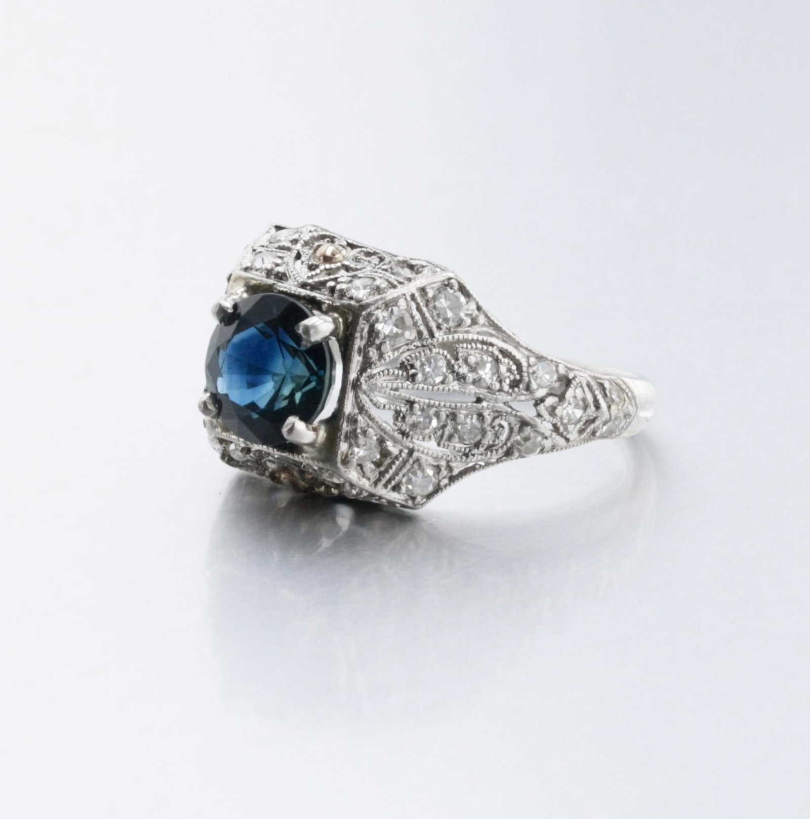Ladies Platinum Filigree Sapphire Ring: Description: A platinum Art Deco diamond ring set with one round 1.46 CT. blue sapphire, good color, set with 42 single-cut diamonds, approx. 0.63 Cts. The top of the ring has pierced filigree heart d