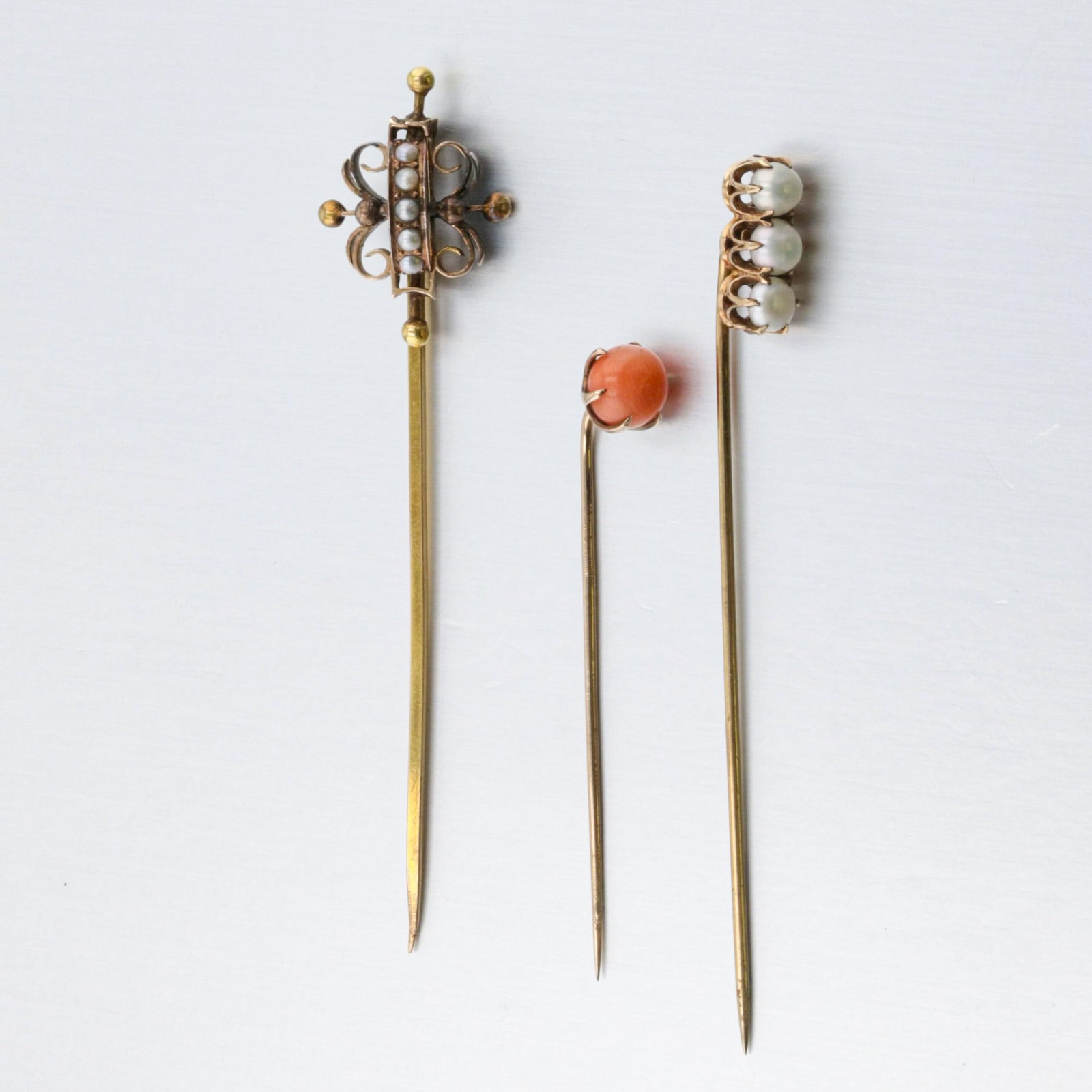 Group Of Three Gold Stick Pins: Description: A group of three low-10K gold stick pins, two set with pearls and one set with a round coral bead. Markings & Inscriptions: None visible. Date: Early to Mid 20th century Maker: Unknown, n