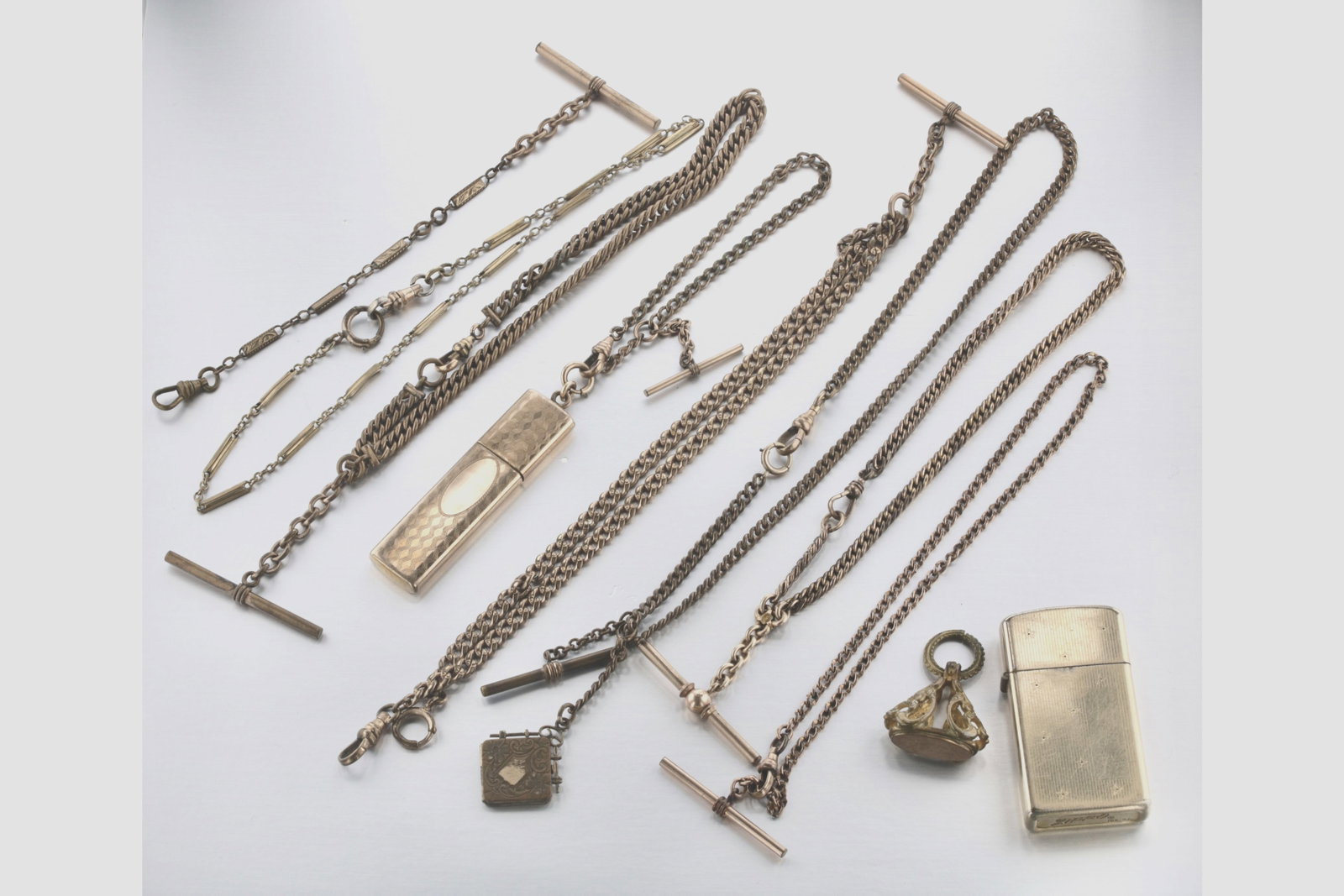 Collection of Vintage Pocket Watch Vest Chains and Acessories: Description: A group of eight pocket watch chains, a gold-filled Zippo lighter, and three fobs. Markings & Inscriptions: GF, 10KGF, and others Date: Early 20th Century Maker: Unknown. Dimensions: The 