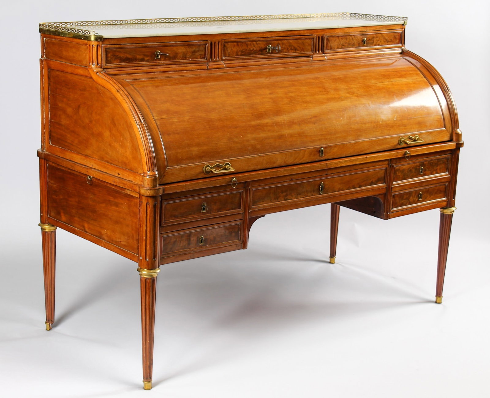 Louis XVI Period Cylinder Desk, Jean-Philippe Feuerstein (French, B. 1749): Description: A Louis XVI cylinder desk in mahogany with a galleried white marble top and a leather writing surface. Bronze-mounted turned and fluted legs on castors support the desk, which contains te