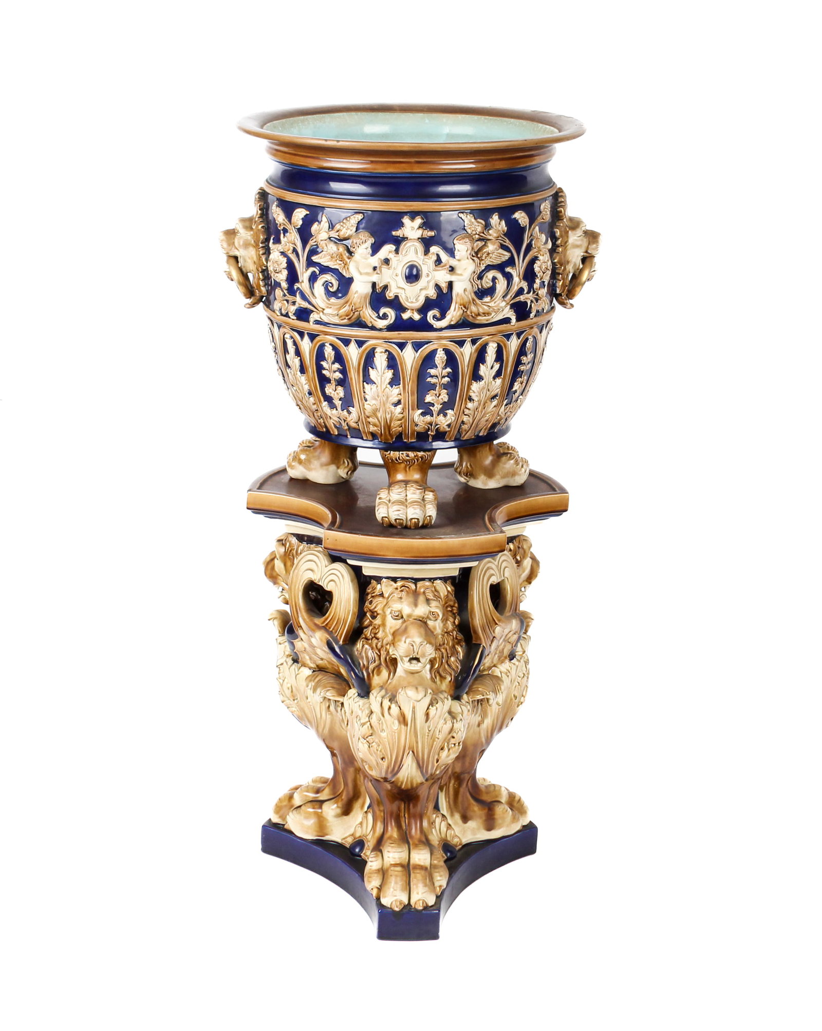 English Majolica Lion-Decorated Jardiniere on Stand: Description: A large English majolica jardiniere on stand, decorated with lion's head and paw foot base and lion's head with gilt ring handles. Markings & Inscriptions: Impressed mark under base Date: