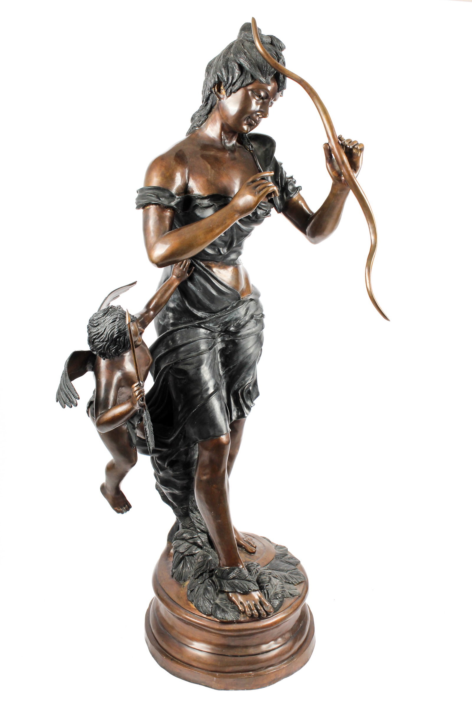 After Alfred Boucher (French, 1850-1934) Bronze Statue of Venus and Cupid: Description: Patinated and cold-painted bronze statue of Venus and Cupid after Alfred Boucher. Venus clad in a draped garment and holding a bow and Cupid holding an arrow. All on a round, bronze, plin