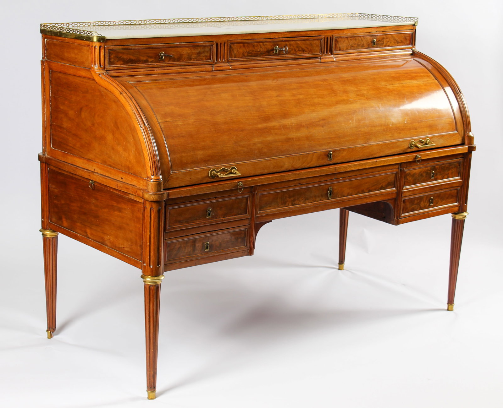 Louis XVI Period Cylinder Desk, Jean-Philippe Feuerstein (French, B. 1749): Description: A Louis XVI cylinder desk in mahogany with a galleried white marble top and a leather writing surface. Bronze-mounted turned and fluted legs on castors support the desk, which contains te