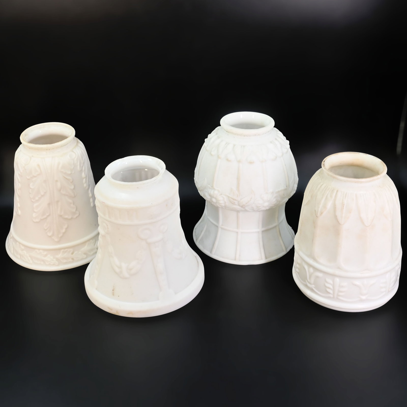 Group of four beautifully ornate leafy 2 1/4" fitter white glass shades: Group of four beautifully ornate leafy 2 1/4" fitter white glass shades. Left: 5" tall x 5" diameter. Middle Left: 5" tall x 4 3/4" diameter. Middle Right: 5 1/2" tall x 4 1/2" diameter. Right: 5" tal
