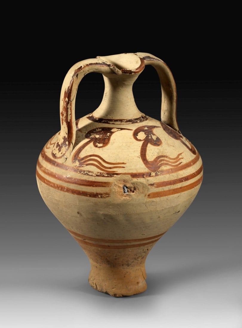 Minoische Amphora mit Bügelhenkeln.: Minoan stirrup amphora. Late Minoan II, 15th - 14th century BC. Height 17,2cm, ø corpus 11,8cm. Reddish to dark brown painting. On the shoulder six three-stemmed ivy-leaves. Two large surficial chipp