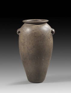 Schlanke Steinvase aus Grauwacke.: Brown-black greywacke vase. Elegant, elongated ovoid body with a flat base, narrow, horizontal lip, and horizontal, elongated eyelets. Early Dynastic Period, ca. 3300 - 2900 BC. Missing part and small