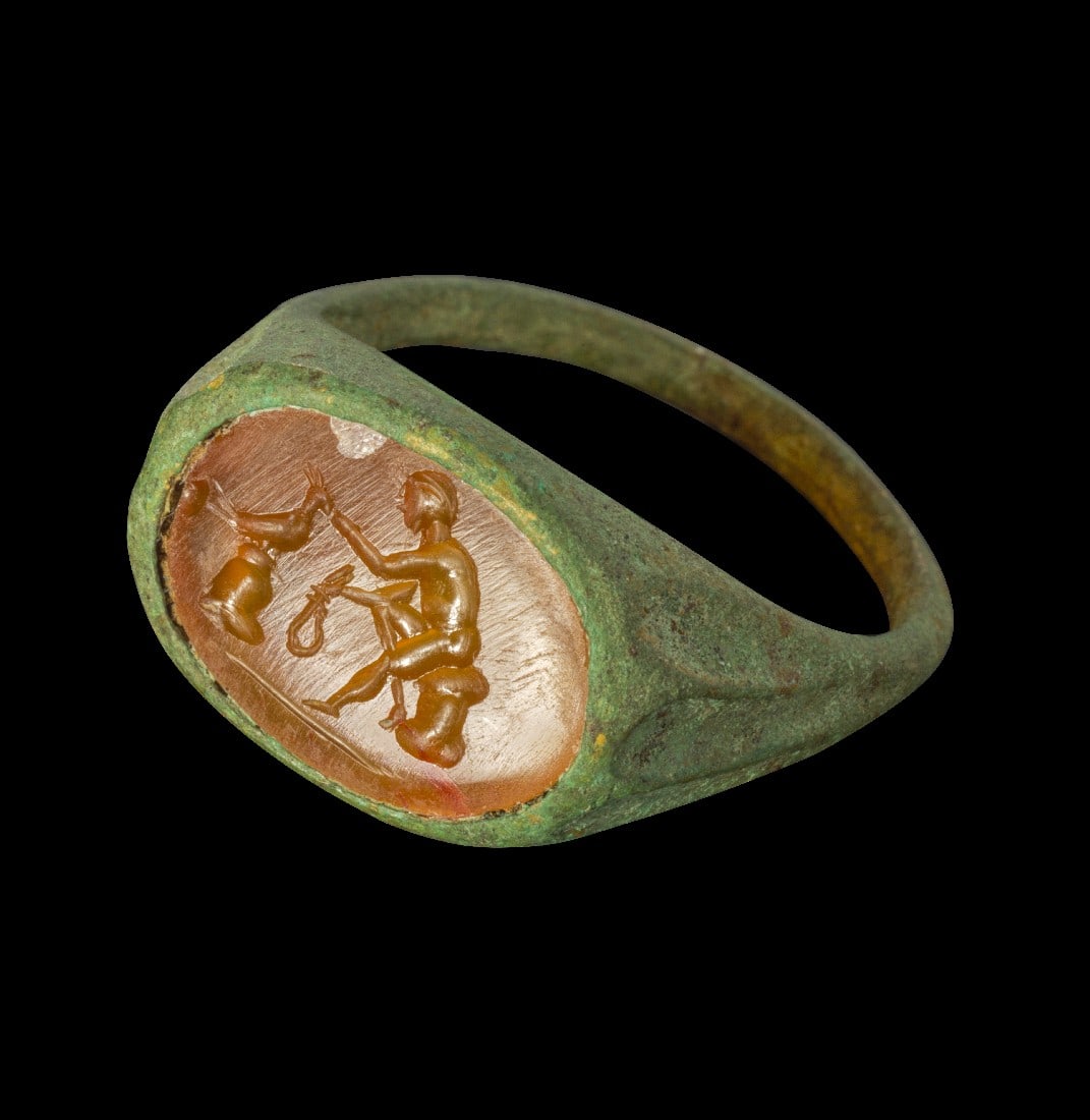 Moderner Bronzering mit antiker Karneolgemme.: Modern bronze ring with ancient cornelian gemstone depicting a naked, sitting man with a lasso, in front of him a peacock on a stand, ringsize 9.9 (US), T 1/2 (UK), 22 (F).Fingerring modern, 20th cent