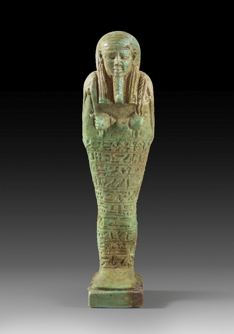 Uschebti für General Ankh-Wahibre-Sa-Neith.: Uschebti für General Ankh-Wahibre-Sa-Neith. Spätzeit, 26. Dynastie, 664 - 525 v. Chr. H 18cm. Hellgrüne Fayence. Mumienförmig mit dreigeteilter Perücke, Bart und Hacke und Pflug. Auf der