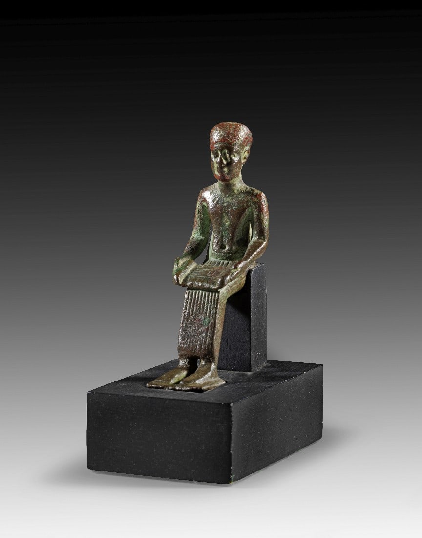 Statuette des Imhotep.: Statuette des Imhotep. Spätzeit, 26. Dynastie, 664 - 525 v. Chr. H 8cm, mit Sockel 10,5cm. Bronzevollguss. Sitzende Statuette des Imhotep mit langem Schurz, Halskragen und Haube, auf den Knien eine