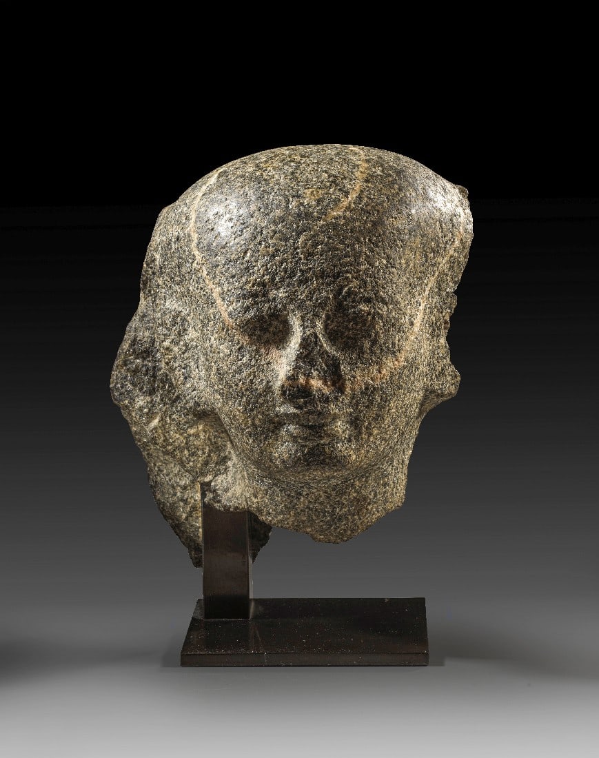 Priesterkopf.: Priesterkopf. Ptolemäisch, ca. 332 - 30 v. Chr. Granit, H 25,5cm. Das Bildnis zeigt einen leise lächelnden jugendlichen Mann, der ein Kopftuch über einer Perücke trägt. Das Stück ist