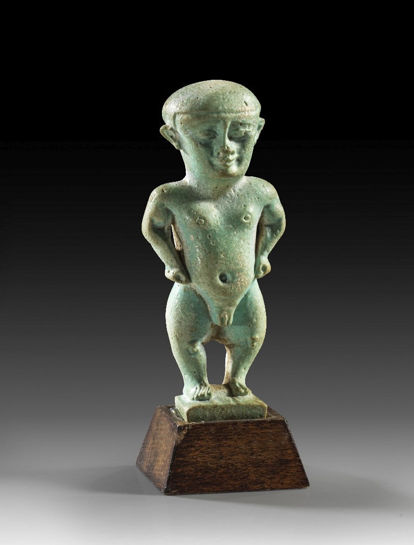Patäke.: Patäke. Spätzeit, 26. - 30. Dynastie, 664 - 343 v. Chr. H 7,8cm, mit Sockel 9,5cm. Fayence. Statuette eines Patäken (naturgetreue Wiedergabe eines kleinwüchsigen Menschen), der die Hände in die