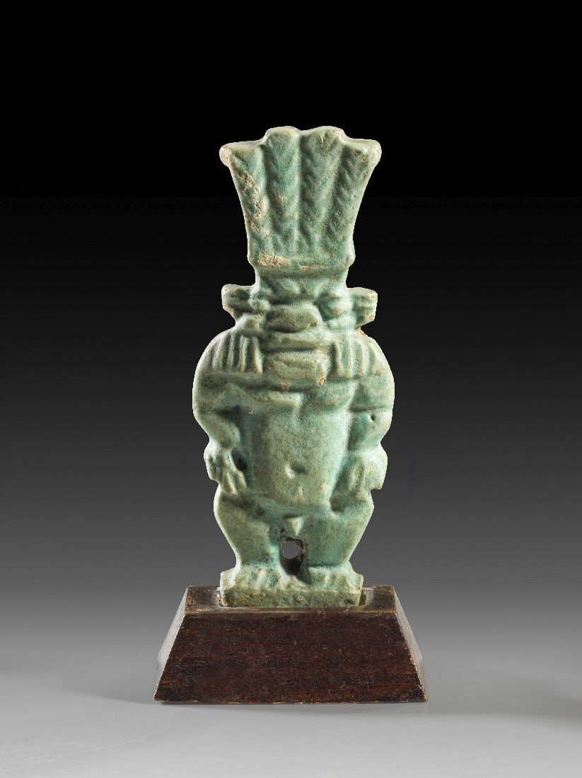 Bes-Amulett.: Bes-Amulett. Spätzeit, 26. - 30. Dynastie, 664 - 343 v. Chr. H 7,6cm, mit Sockel 9,0cm. Fayence. Zwergenartiger Gott Bes mit hoher Federkrone. Der Kopfschmuck ist unten längs durchbohrt, um die