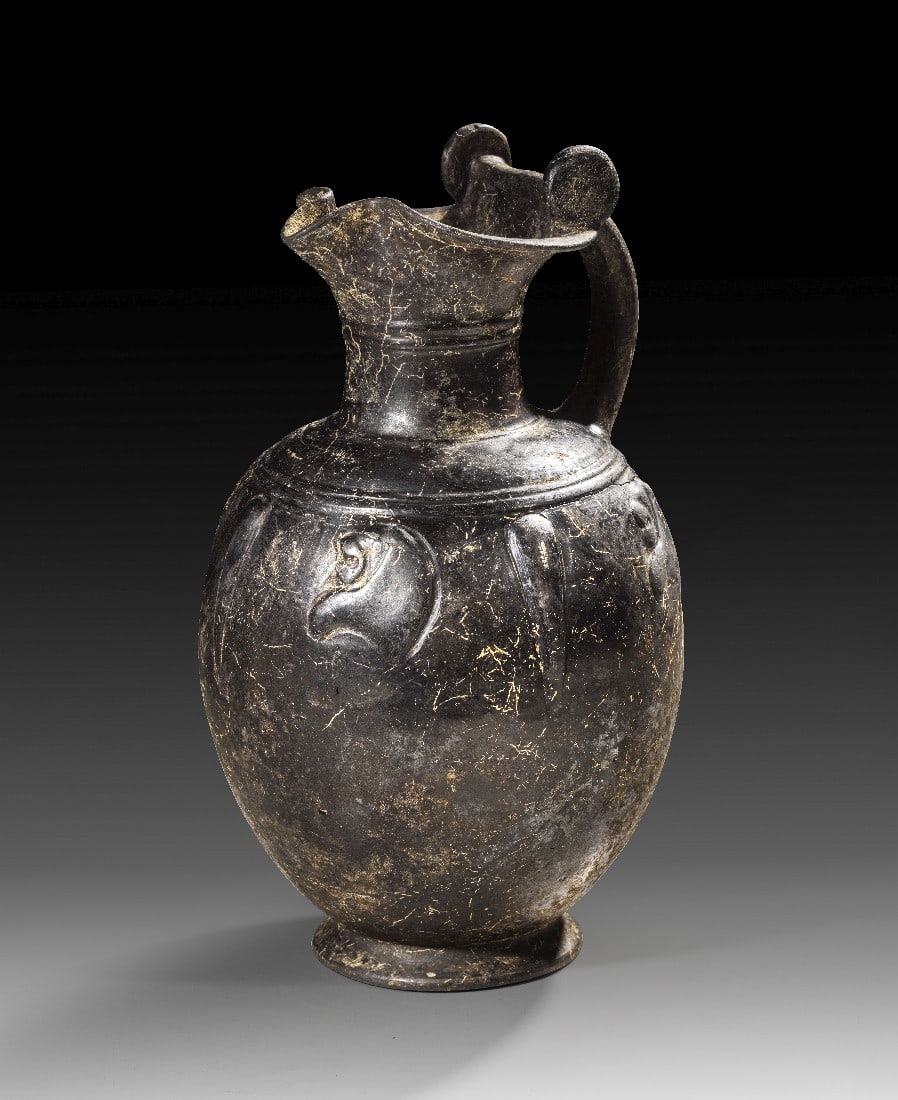 Etruskische Bucchero-Oinochoe.: Etruskische Bucchero-Oinochoe. 575 - 550 v. Chr. H 30,6cm, ø 17,7cm. Kanne aus Bucchero pesante mit plastischem Dekor, Kleeblattmündung und Rotellenhenkel. Auf dem Körper zwischen Lanzettblättern