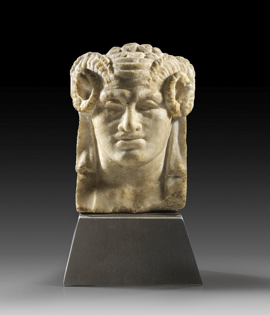 Zeus Ammon.: Zeus Ammon. Römische Kaiserzeit, 1. - 2. Jh. n. Chr. H 18,5cm, T 6cm. Weißer, etwas grobkristalliner Marmor. Flacher, frontaler Reliefkopf von einer Herme. Dargestellt ist ein bartloser,