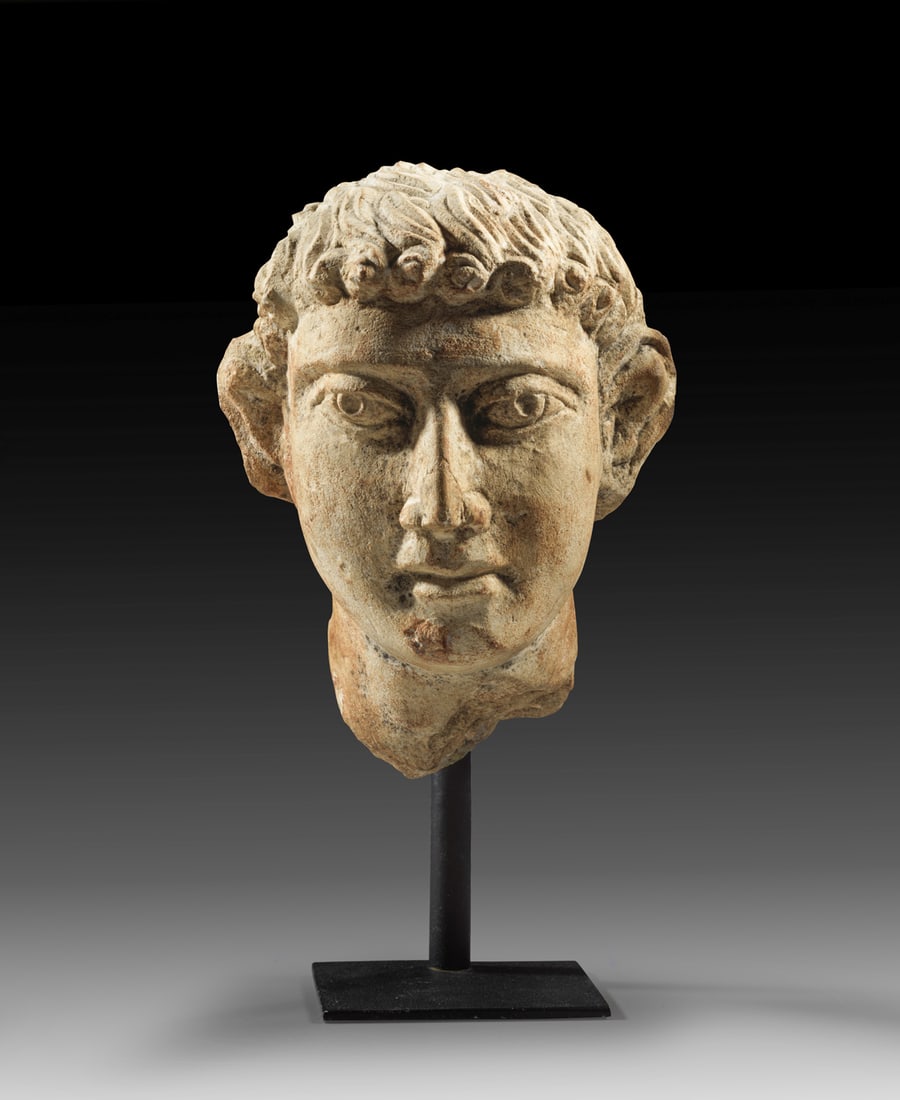 Römischer Kopf eines jungen Mannes aus Kalkstein.: Römischer Kopf eines jungen Mannes aus Kalkstein. Östlicher Mittelmeerraum, ca. Mitte des 3. Jhs. n. Chr. H 17,2cm und mit Ständer 23,6cm. Unterlebensgroßer, schmaler Kopf mit abstehenden Ohren.