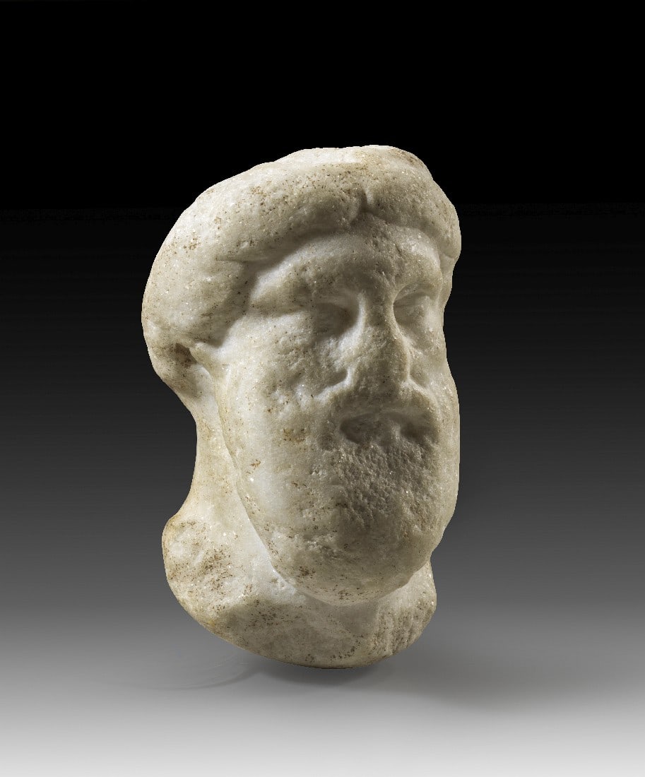 Kopf des Hermes oder Dionysos.: Kopf des Hermes oder Dionysos. Römische Kaiserzeit, 1. - 2. Jh. n. Chr. H 12cm. Weißer, feinkristalliner, pulvrig-glitzernder Marmor. Fast vollplastischer Reliefkopf vermutlich von einer Herme. Der