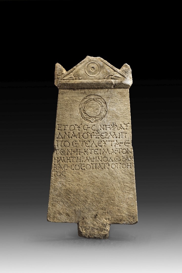 Grabstele mit Giebel, Lorbeerkranz und griechischer Inschrift.: Grabstele mit Giebel, Lorbeerkranz und griechischer Inschrift. Römisch, östliches Mittelmeergebiet, 7. Dezember 168 n. Chr. H 60cm, B unten 30cm, T 5cm. Weißer Marmor. Platte, deren Längskanten