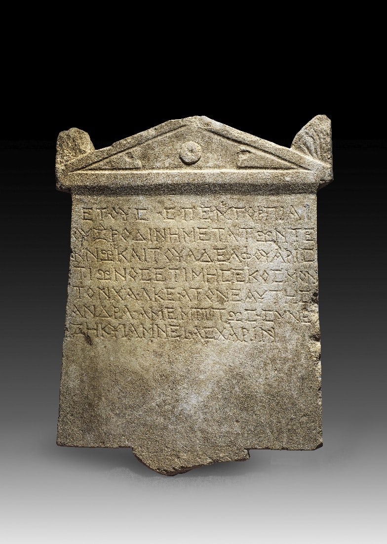 Grabstein mit Giebel und griechischer Inschrift.: Grabstein mit Giebel und griechischer Inschrift. Römisch, östliches Mittelmeergebiet, 2. - 3. Jh. n. Chr. H 61cm, B unten 45cm, T 6,5cm. Marmor. Platte, deren Längskanten leicht konisch verlaufen