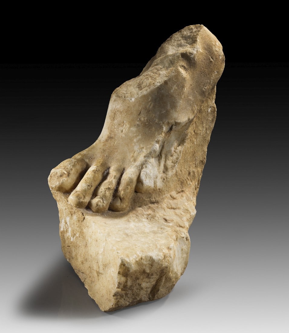 Fuß einer Statue.: Fuß einer Statue. Römische Kaiserzeit, wohl 2. - 3.Jh n. Chr. H 24cm, L 38cm. Feinkristalliner weißer Marmor. Fragment einer Plinthe mit leicht angehobenem linken Fuß. Fragmentarisch. Provenienz: