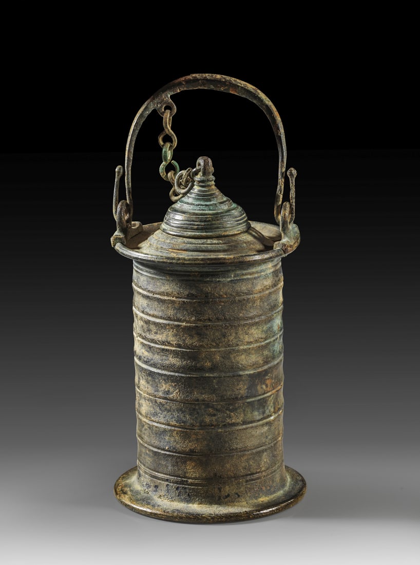 Tintenfass aus Bronze.: Tintenfass aus Bronze. Römisch, 1. Jh. n. Chr. H mit Henkel 17cm, H Corpus ohne Deckel 10cm, ø 7,5cm. Flache Bodenplatte mit konzentrischen Kreisen auf der Unterseite, zylindrischer Corpus mit