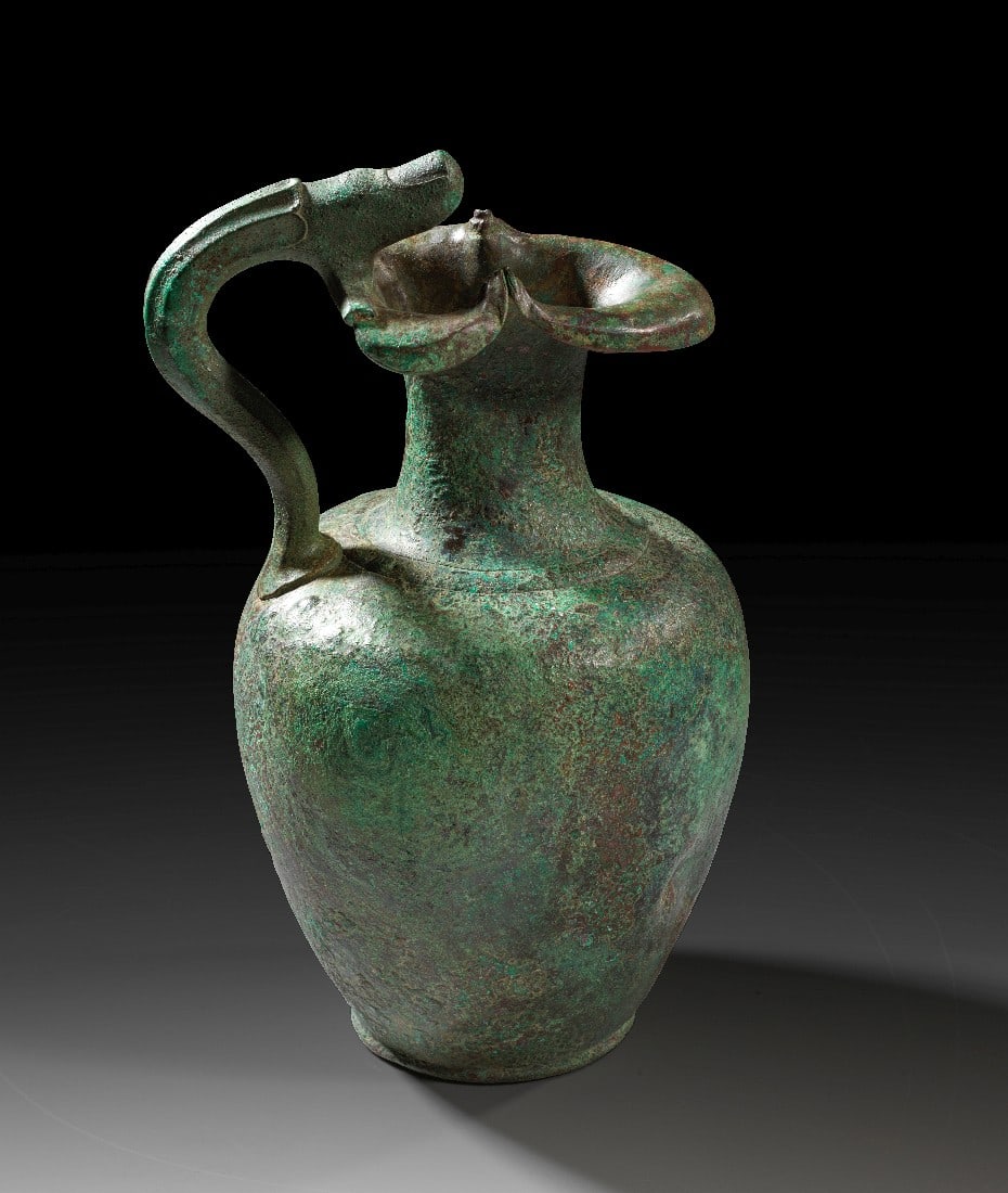 Römische bronzene Kleeblattkanne mit figürlichen Henkel.: Römische bronzene Kleeblattkanne mit figürlichen Henkel. Frühe Kaiserzeit, Ende 1. Jh. v. Chr. - 1. Jh. n. Chr. H 24,6cm, ø 13,8cm. Körper aus Bronzeblech, Fuß und Henkel aus Vollguss. Der