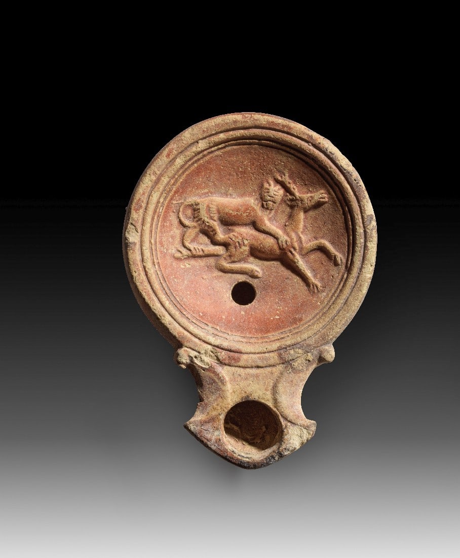Römische Tonlampe mit Löwe und Hirsch.: Römische Tonlampe mit Löwe und Hirsch. Kaiserzeitlich, 1. - 2. Jh. n. Chr. L 9,5cm. Typus Loeschcke IV. Hellbeiger Ton mit rötlichem Überzug. Auf dem Spiegel greift ein Löwe von hinten einen