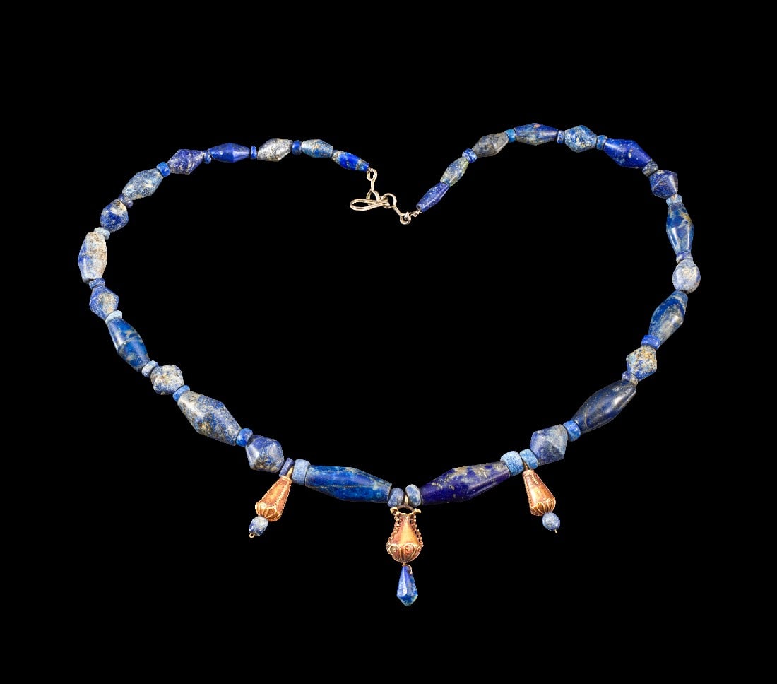 Kette aus Lapislazuli-Perlen.: Kette aus Lapislazuli-Perlen. Westasiatisch, 2. Jt. v. Chr. L 49,5cm. Aus bikonischen Röhrenperlen und Scheibenperlen. Zentral eine Goldperle in Form eines Gefäßes und zwei tropfenförmige