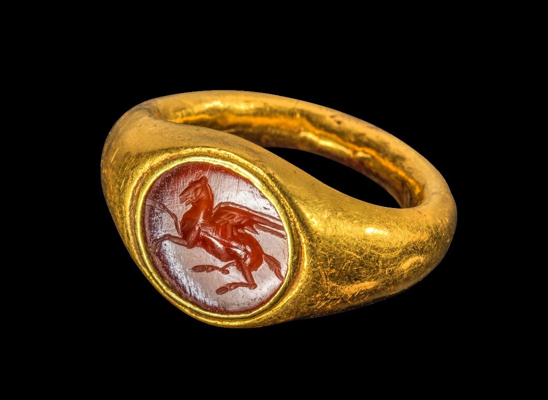 Goldring mit Pegasos.: Goldring mit Pegasos. Römisch, 1. - 2. Jh. n. Chr. 4,99g, Ringgröße 48. Nach oben breiter werdender Schiene, auf der Platte eingelassen eine querovale Gemme aus orangem Karneol mit einem