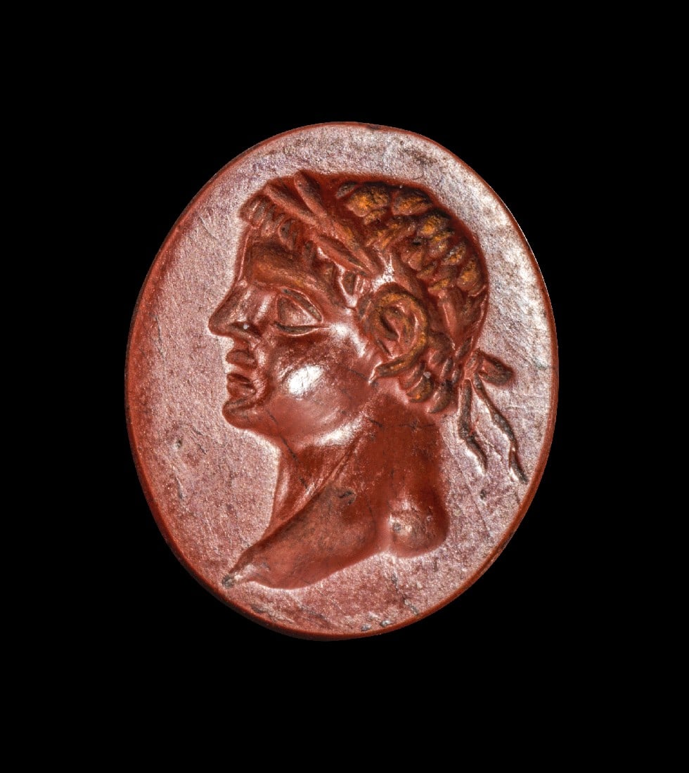 Japsisgemme mit kaiserlichem Prinzen.: Japsisgemme mit kaiserlichem Prinzen. Frühe Kaiserzeit, Anfang 1. Jh. n. Chr. 1,6 x 1,3cm. Flaches Intaglio aus rotem Jaspis. Kopf eines jugendlichen Caesars mit Lorbeerkranz. Intakt. Provenienz: