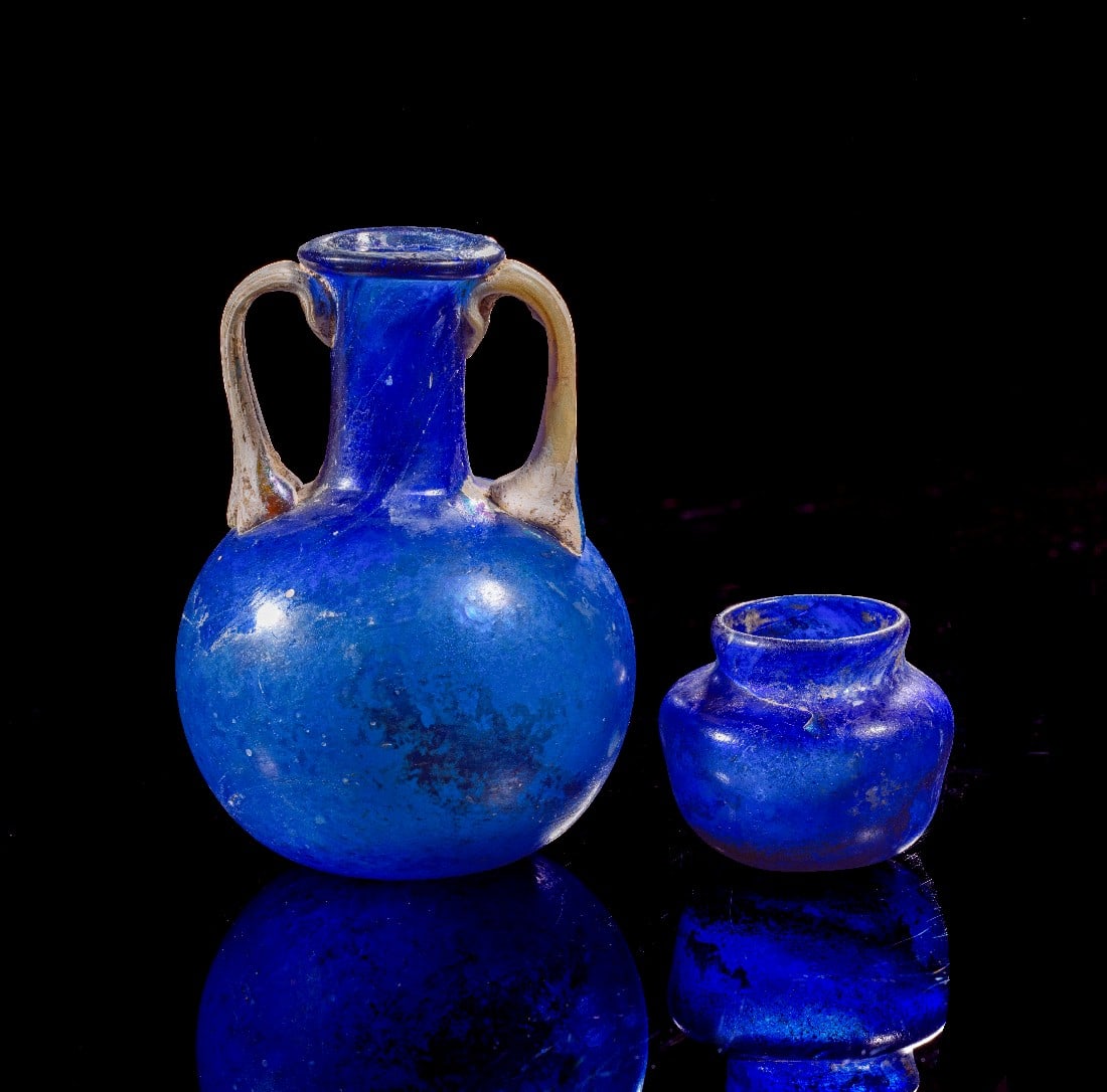 Zwei blaue Gläser.: Zwei blaue Gläser. Römische Kaiserzeit, 1. Jh. n. Chr. Ein blauer Amphoriskos mit kugeligem Corpus und zwei weißen Henkeln. Sprung in einem Henkel, H 9cm. Dazu ein apfelförmiges Töpfchen aus