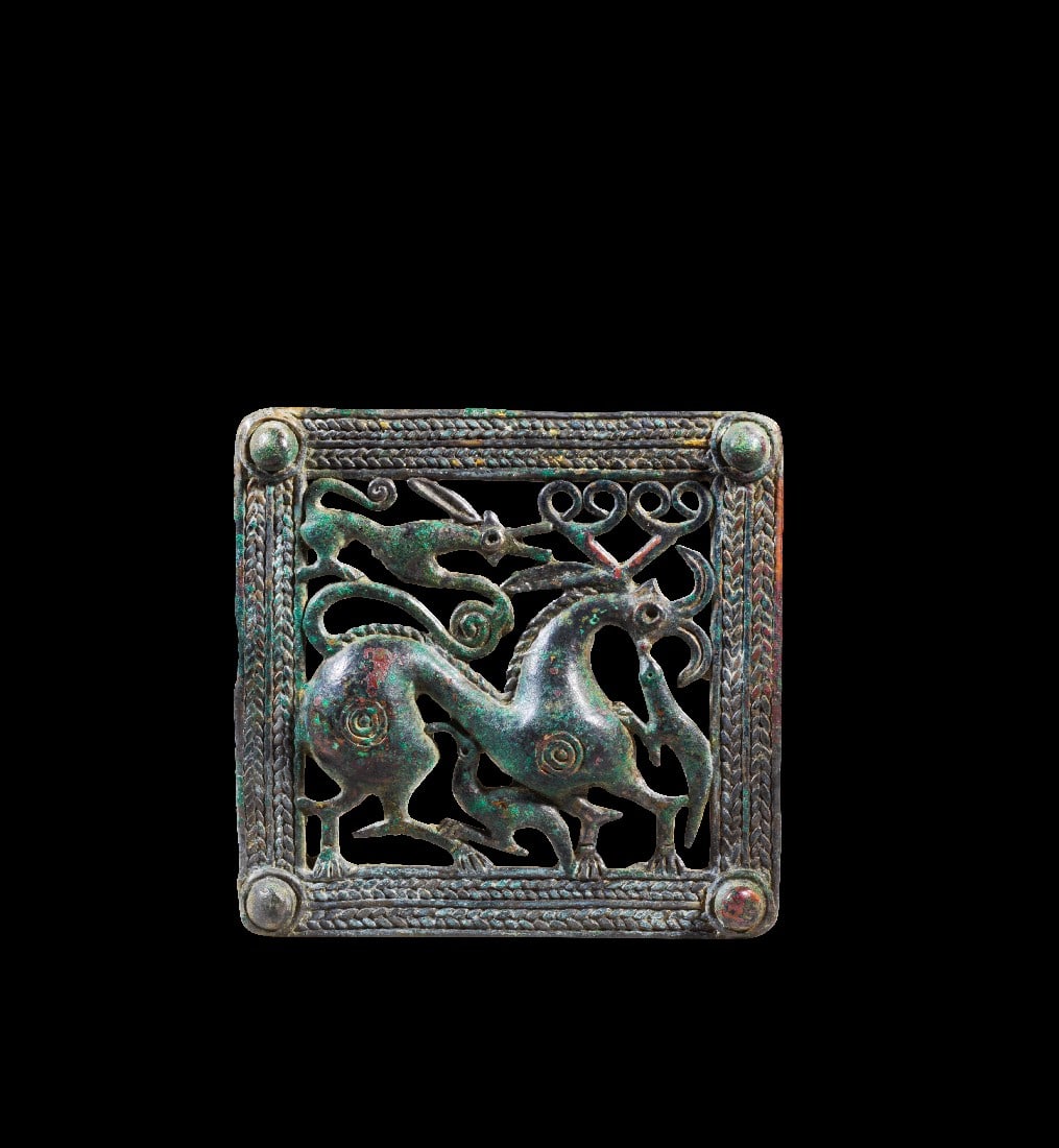 Gürtelschließe mit Tierkampf.: Gürtelschließe mit Tierkampf. Transkaukasien, 1. - 3. Jh. n. Chr. H 10,2cm B 10,5cm. Bronzeguss. Quadratisches Relief mit einem Rahmen aus Flechtbändern mit konischen Knubben an den Ecken. Das
