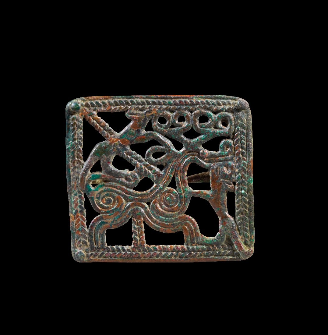 Gürtelschließe mit Tierkampf.: Gürtelschließe mit Tierkampf. Transkaukasien, 1. - 3. Jh. n. Chr. H 8,2cm B 9cm. Bronzeguss. Quadratisches Relief mit einem Rahmen aus Flechtbändern. Das Bildfeld ist durchbrochen gearbeitet und