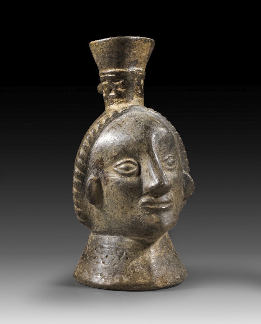 Kopfgefäß.: Kopfgefäß. Moche, ca. 450 - 600 n. Chr. H 17cm. Gefäß in Form eines schmalen Kopfes mit mandelförmigen Augen. Vertiefter stufenförmiger Dekor am Ausguss und am Hals. Griff abgebrochen,