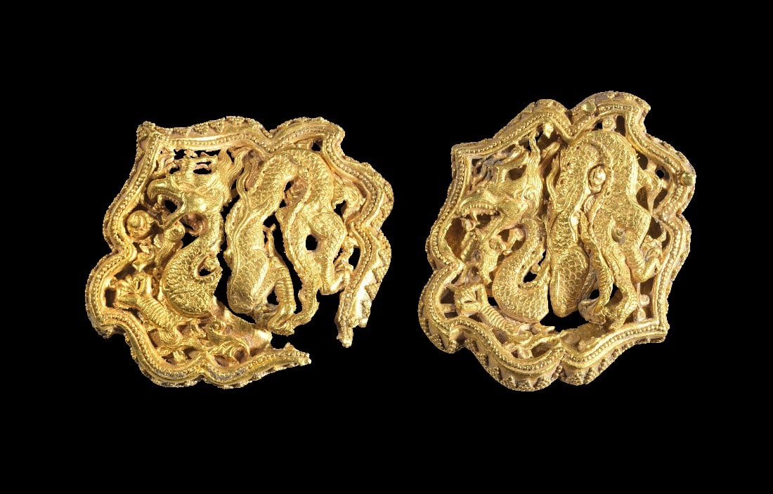 Zwei Goldappliken mit Drachenmotiv.: Zwei Goldappliken mit Drachenmotiv. China. 59,36g, B 6cm, H 5 u. 5,5cm. Zwei ineinander verschlungene Drachen durchbrochen gearbeitet in einem Rahmen mit Granulatdekor, auf der Rückseite Goldblech