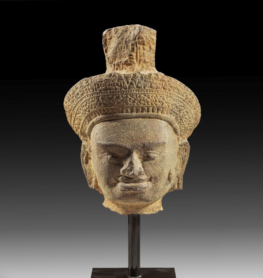 Kleiner Khmer Kopf einer männlichen Gottheit, wohl Vishnu.: Kleiner Khmer Kopf einer männlichen Gottheit, wohl Vishnu. Südostasien, Angkor Vat, um 1100 n. Chr. H 28cm und mit Sockel 42cm. Sandstein mit feiner grauer-gelber Gesteinspatina. Erlesener Kopf