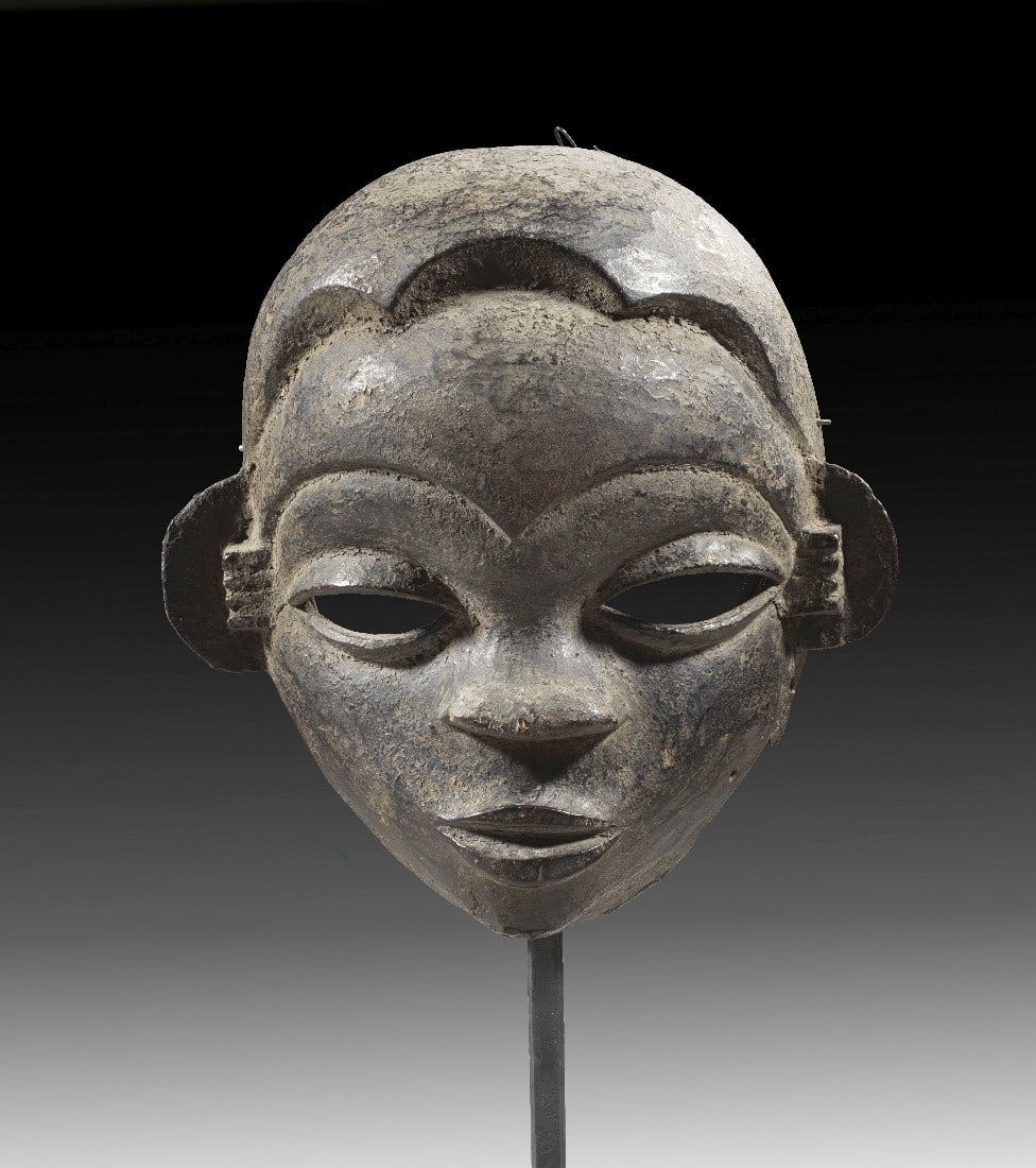 Ibibio-Maske.: Ibibio-Maske. Nigeria. H 21,5cm. Holz. Mit Metallständer. Gesicht mit abstehenden Ohren, breiter Nase und wulstigen Lippen. Krustenpatina, Fragmente am Rand fehlen. Provenienz: Ex Sammlung Dr. Vera