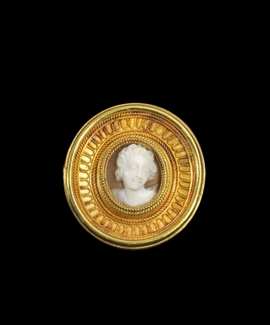 Goldbrosche von Castellani.: Goldbrosche von Castellani. Europa, 19. Jh. 6,54g, ø 23mm. Runde Brosche aus Gelbgold mit einem Kameo in der Mitte, der die Büste einer Frau im Dreiviertelprofil darstellt. Feine Körnungen aus