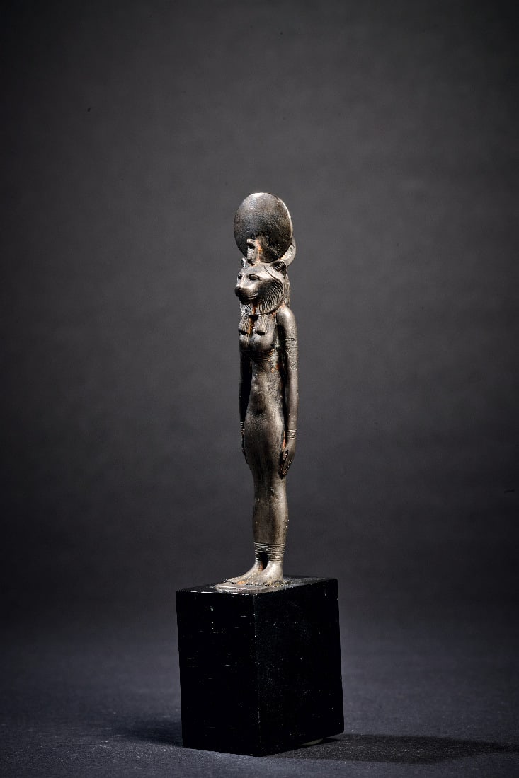 Silberfigur der Sachmet.: Silberfigur der Sachmet. Neues Reich, 18. Dynastie, um 1400 v. Chr. Amulett aus massivem Silber. H 8cm (ohne Basis). Stehende, loewenkoepfige Goettin in enganliegendem Gewand. An den Armen und an der 