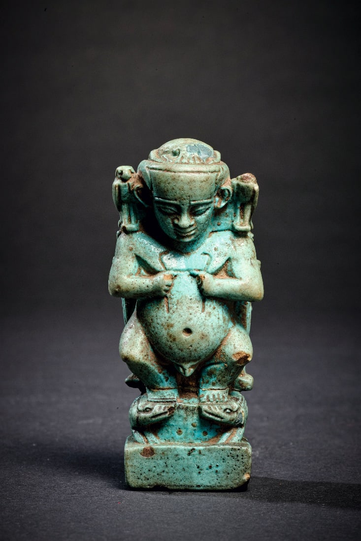 Pataeke.: Pataeke. Spaetzeit, wohl 26. Dynastie, ca. 664 - 525 v. Chr. Blaue Fayence, H 7,7cm. Grosses Amulett in Form des auf zwei Krokodilen stehenden Pataeken, der in jeder Hand eine Schlange haelt. Auf sein