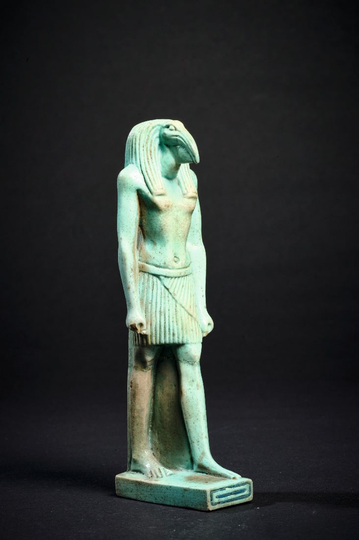 Praechtige Statuette des Gottes Thot.: Praechtige Statuette des Gottes Thot. Spaetzeit, ca. 525 - 332 v. Chr. H ca. 12cm (ohne Sockel). Tuerkise Fayence. Ibiskoepfiger Gott im Schurz, auf Plinthe stehend, das linke Bein vorgestellt, Ruecke
