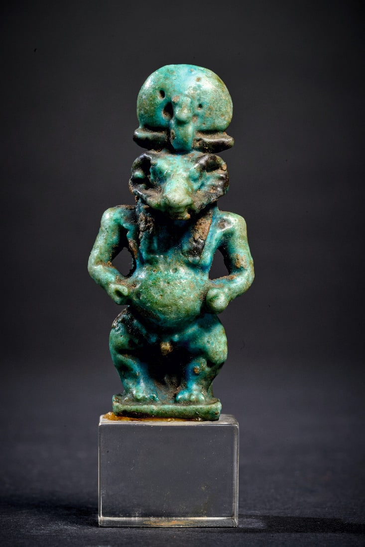 Chnum.: Chnum. Ptolemaeerzeit, ca. 323 - 30 v. Chr. H 5,2cm. Amulett aus dunkelgruener und schwarzer Fayence. Pataeke mit Widderkopf und Sonnenscheibe. Auf der Rueckseite gefluegelte Hathor im Relief. Zweifar