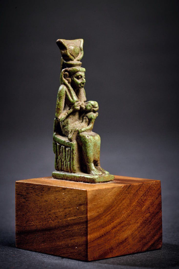 Amulett der Isis mit Horusknaben.: Amulett der Isis mit Horusknaben. Spaetzeit, 664 - 332 v. Chr. H 6cm (mit Sockel), H 4cm (ohne Sockel). Aus gruenlicher Fayence. Thronende Isis mit Kuhgehoern und Sonnenscheibe, die dem auf ihrem