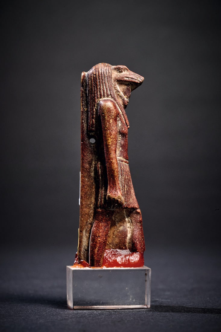 Amulett des Gottes Thot.: Amulett des Gottes Thot. Spaetzeit, ca. 525 - 332 v. Chr. H 6cm (ohne Sockel). Auberginefarbene Fayence. Ibiskoepfiger Gott im Schurz, auf Plinthe stehend, das linke Bein vorgestellt, Rueckenpfeiler